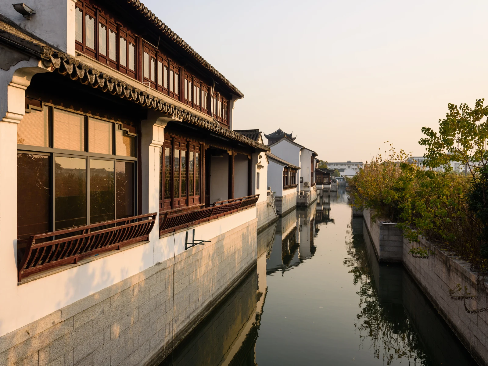 Traditional white walls and timber balconies along a Suzhou canal in warm evening light