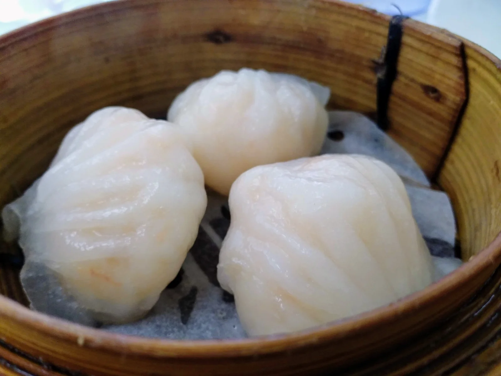 Three translucent shrimp dumplings in a bamboo basket