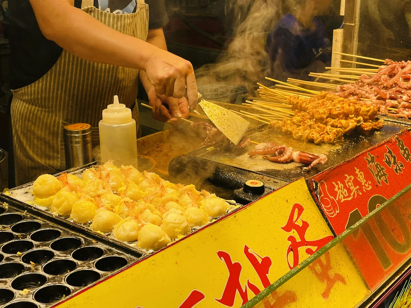 A cook grilling squid and seafood skewers at a street-food stall in Xiamen